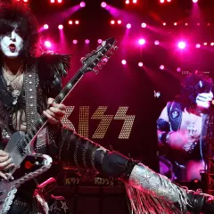 Paul Stanley dei KISS con la sua chitarra, luci rosa e il logo della band. Un momento iconico per chi ama il rock.
