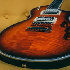 Chitarra rock con finitura fiammata arancione e nera, appoggiata su un divano giallo ocra.