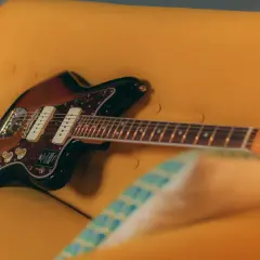 Chitarra Fender Jazzmaster color sunburst appoggiata su un divano giallo. Un duello tra jaguar e jazzmaster, quale suono preferisci?