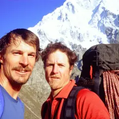 Due escursionisti sorridono con uno zaino e una corda da arrampicata, pronti a haken the mountain innevata sullo sfondo.