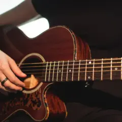 Mano che suona una chitarra acustica Takamine, con dettagli in tartaruga. Le opinioni su queste chitarre sono ottime.