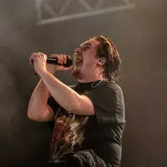Cantante con microfono, la sua espressione è intensa, quasi un'ombra di intento.