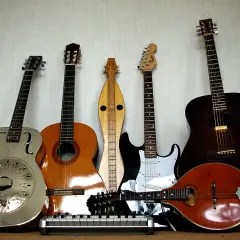 Una collezione di chitarre, tra cui una chitarra in metallo lucido, una acustica, una elettrica e un mandolino.