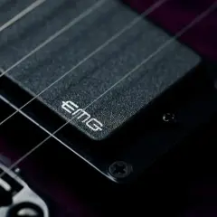 Dettaglio di una chitarra elettrica con pickup attivi EMG. Le corde metalliche brillano sopra il pickup nero.
