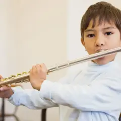 Bambino suona il flauto, uno strumento che si suona con le mani, con espressione concentrata.