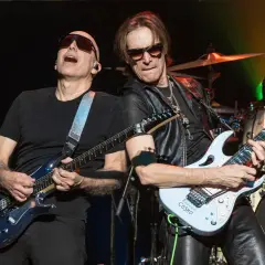 Joe Satriani e Steve Vai, due leggende della chitarra, suonano insieme sul palco. La band di Steve Vai è in piena azione.
