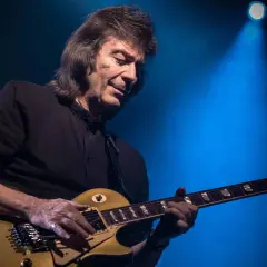 Steve Hackett, ex chitarrista dei Genesis, suona la sua chitarra dorata sotto un fascio di luce blu.