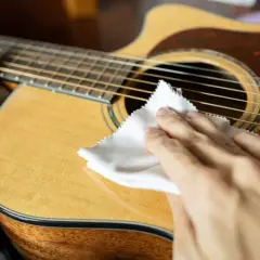 Mani che puliscono la chitarra classica con un panno bianco, un gesto essenziale per la cura dello strumento.
