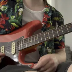 Un chitarrista con una camicia floreale suona una chitarra rossa, ricordando lo stile di Guthrie Govan.