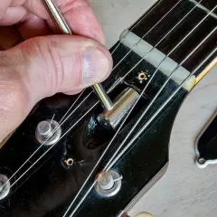 Regolazione del truss rod a doppia azione di una chitarra. La mano usa una chiave per agire sul meccanismo.