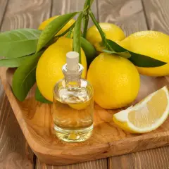 Un flacone di olio di limone chitarra, circondato da limoni freschi e foglie verdi, su un vassoio di legno.
