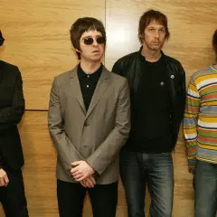 I quattro membri degli Oasis, con i loro look iconici, sembrano pronti per un concerto, un'istantanea degli anni '90.