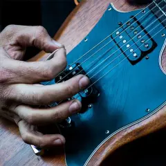 Mano che pizzica le corde di una chitarra elettrica. È più facile suonare la chitarra elettrica o acustica? La risposta è soggettiva.