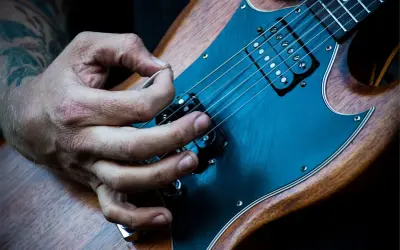 Mano che pizzica le corde di una chitarra elettrica. È più facile suonare la chitarra elettrica o acustica? La risposta è soggettiva.