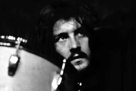 Black and white close-up of John Bonham looking up, with a drum in the foreground.