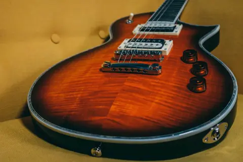 Chitarra rock con finitura fiammata arancione e nera, appoggiata su un divano giallo ocra.