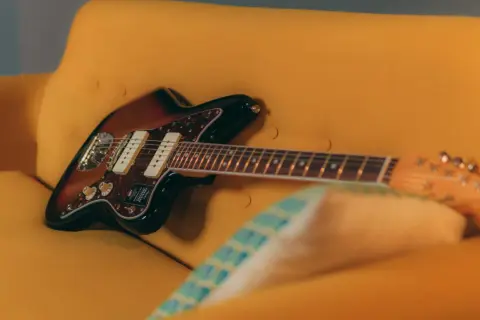 Chitarra Fender Jazzmaster color sunburst appoggiata su un divano giallo. Un duello tra jaguar e jazzmaster, quale suono preferisci?