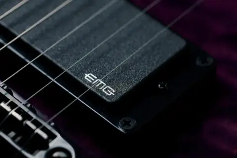 Dettaglio di una chitarra elettrica con pickup attivi EMG. Le corde metalliche brillano sopra il pickup nero.