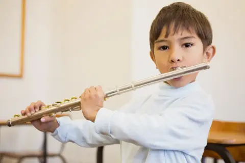 Bambino suona il flauto, uno strumento che si suona con le mani, con espressione concentrata.