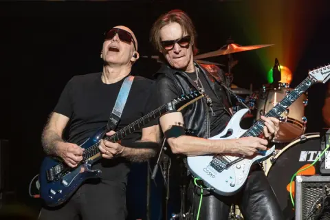 Joe Satriani e Steve Vai, due leggende della chitarra, suonano insieme sul palco. La band di Steve Vai è in piena azione.