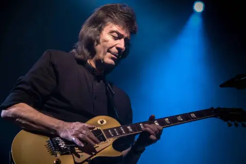 Steve Hackett, ex chitarrista dei Genesis, suona la sua chitarra dorata sotto un fascio di luce blu.
