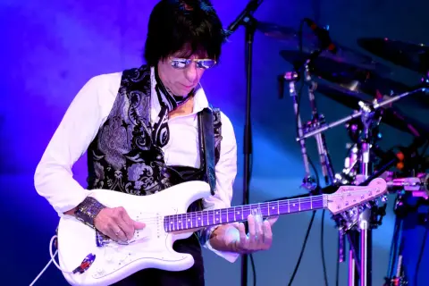 Jeff Beck, con occhiali da sole e gilet decorato, suona la sua chitarra bianca con la band.