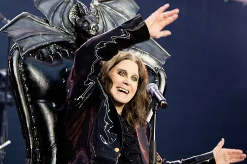 Ozzy Osbourne, icona degli anni '80, canta sul palco con un microfono, dietro di lui un trono demoniaco con ali di pipistrello.