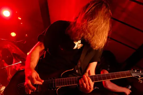 Chitarrista con lunghi capelli biondi, immerso nella luce rossa, crea la base ritmica di un brano con la sua chitarra elettrica.