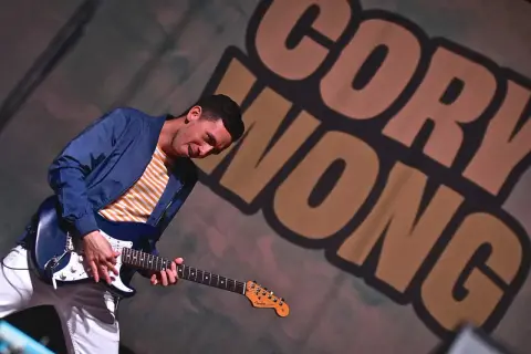 Cory Wong, chitarrista energico, suona la sua Fender con passione. Sullo sfondo, il suo nome in grandi lettere.