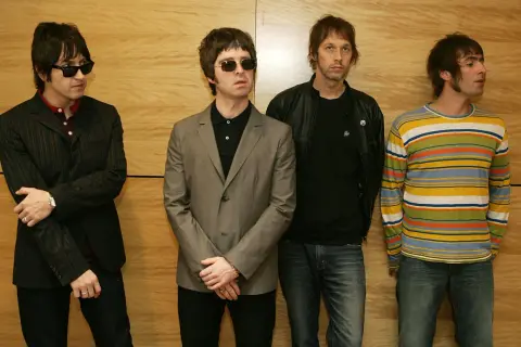 I quattro membri degli Oasis, con i loro look iconici, sembrano pronti per un concerto, un'istantanea degli anni '90.