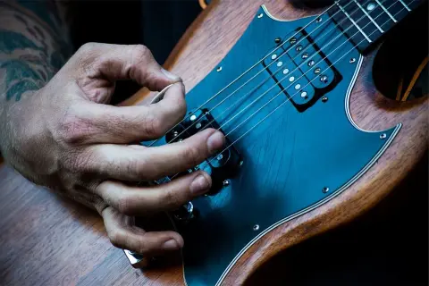 Mano che pizzica le corde di una chitarra elettrica. È più facile suonare la chitarra elettrica o acustica? La risposta è soggettiva.