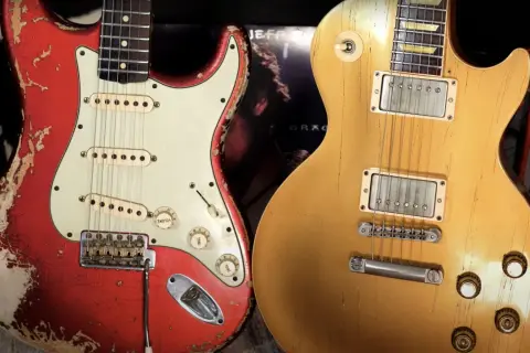 Iconiche chitarre: una Fender rossa consumata e una Gibson dorata, pronte per un duello musicale.