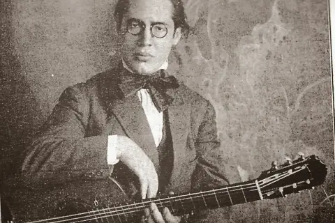 Ritratto di Andrés Segovia, chitarrista, con occhiali rotondi e papillon, mentre suona la sua chitarra.