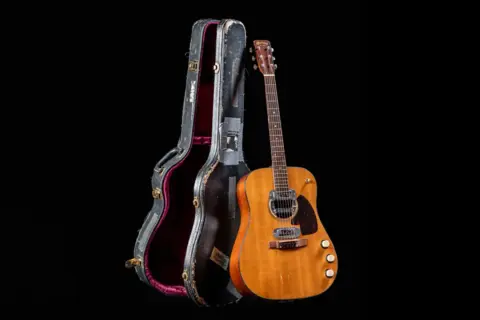 La chitarra acustica di Kurt Cobain, con la sua custodia vissuta, pronta per nuove melodie.