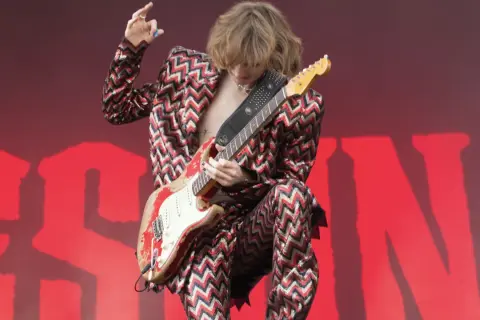 Thomas Raggi, chitarrista dei Måneskin, con la sua iconica chitarra rossa e un completo a zig-zag, infiamma il palco con la sua energia.