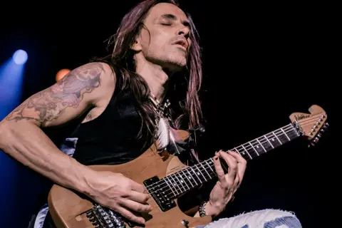 Nuno Bettencourt oggi, con occhi chiusi e capelli lunghi, suona la sua chitarra Washburn con passione.