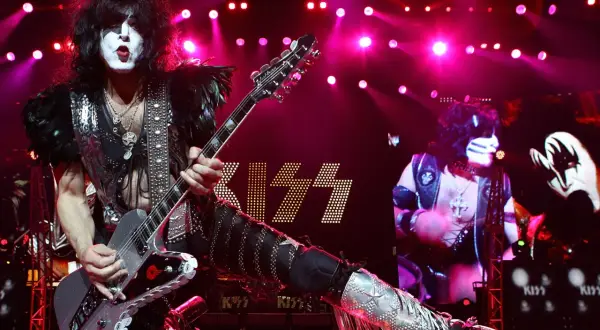 Paul Stanley dei KISS con la sua chitarra, luci rosa e il logo della band. Un momento iconico per chi ama il rock.