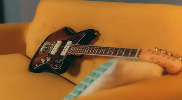 Chitarra Fender Jazzmaster color sunburst appoggiata su un divano giallo. Un duello tra jaguar e jazzmaster, quale suono preferisci?