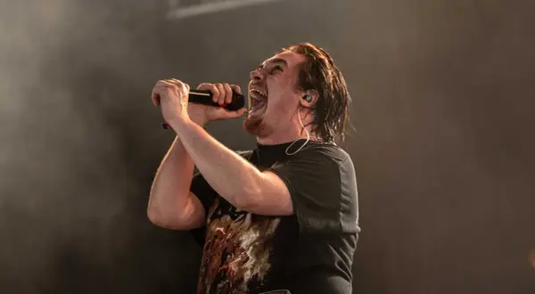Cantante con microfono, la sua espressione è intensa, quasi un'ombra di intento.