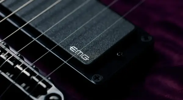 Dettaglio di una chitarra elettrica con pickup attivi EMG. Le corde metalliche brillano sopra il pickup nero.