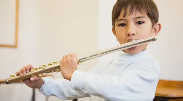 Bambino suona il flauto, uno strumento che si suona con le mani, con espressione concentrata.