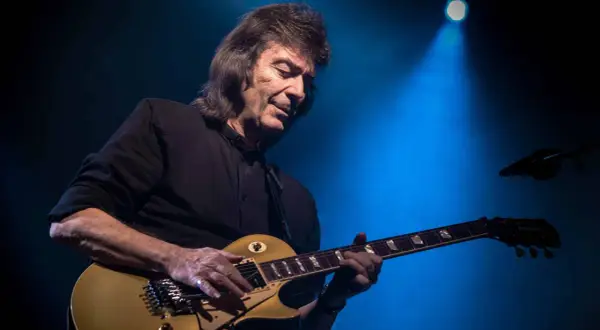 Steve Hackett, ex chitarrista dei Genesis, suona la sua chitarra dorata sotto un fascio di luce blu.