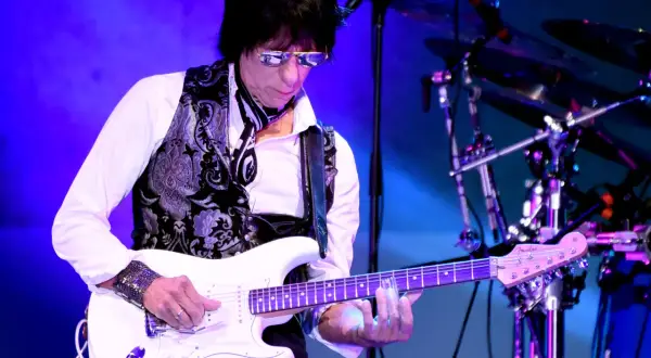 Jeff Beck, con occhiali da sole e gilet decorato, suona la sua chitarra bianca con la band.