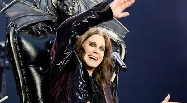 Ozzy Osbourne, icona degli anni '80, canta sul palco con un microfono, dietro di lui un trono demoniaco con ali di pipistrello.