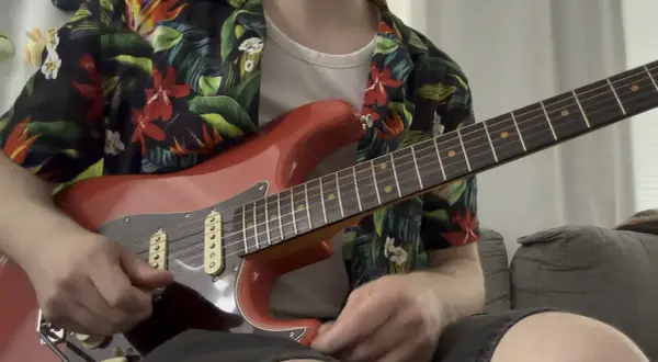 Un chitarrista con una camicia floreale suona una chitarra rossa, ricordando lo stile di Guthrie Govan.