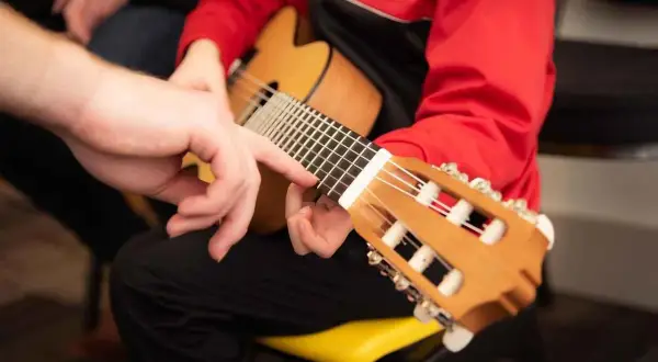 Mano guida un dito sulla tastiera, mostrando la corretta postura chitarra classica.