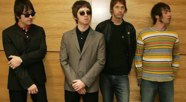 I quattro membri degli Oasis, con i loro look iconici, sembrano pronti per un concerto, un'istantanea degli anni '90.