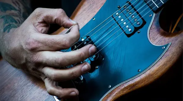 Mano che pizzica le corde di una chitarra elettrica. È più facile suonare la chitarra elettrica o acustica? La risposta è soggettiva.
