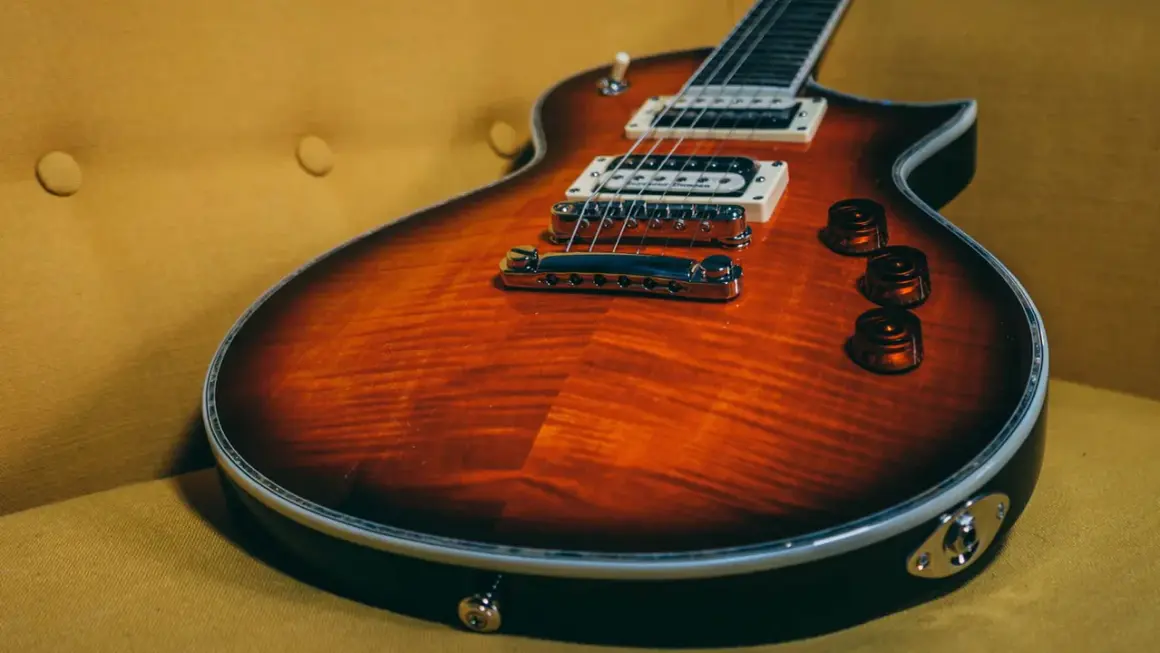 Chitarra rock con finitura fiammata arancione e nera, appoggiata su un divano giallo ocra.