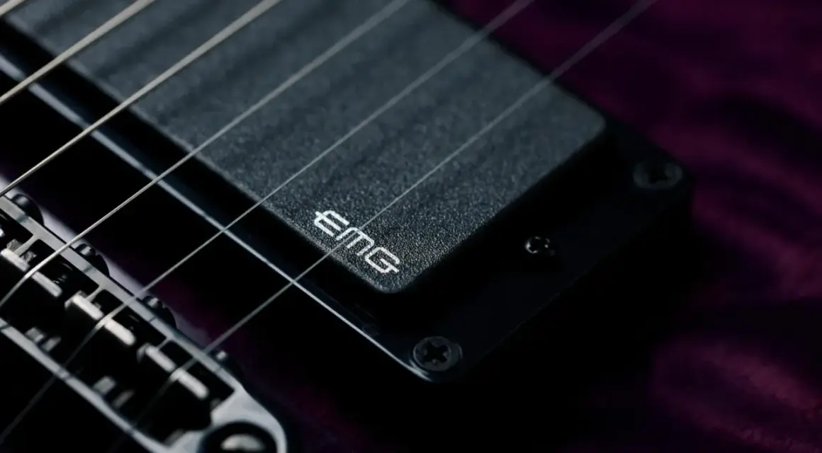 Dettaglio di una chitarra elettrica con pickup attivi EMG. Le corde metalliche brillano sopra il pickup nero.